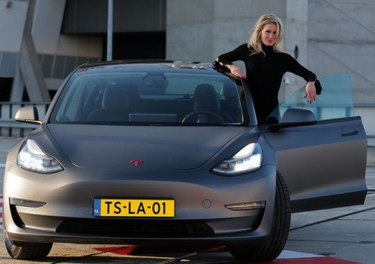 A woman standing on the tesla model 3 vehicle.