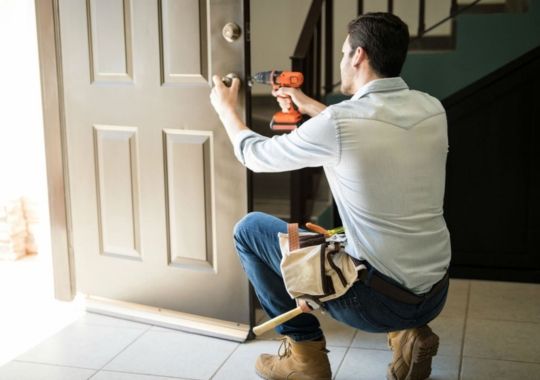A man fixing a door while wearing a tool pouch.